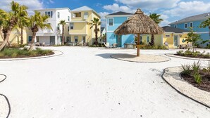 A resort area with a central circular pathway, palm trees, and beach houses with thatched roofs.