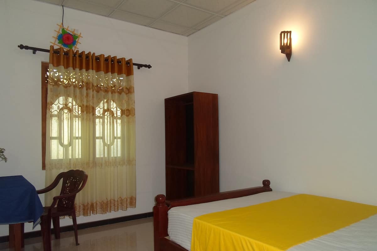 A bedroom with a wooden bed, a small desk with a chair, a wardrobe, and a window with curtains.