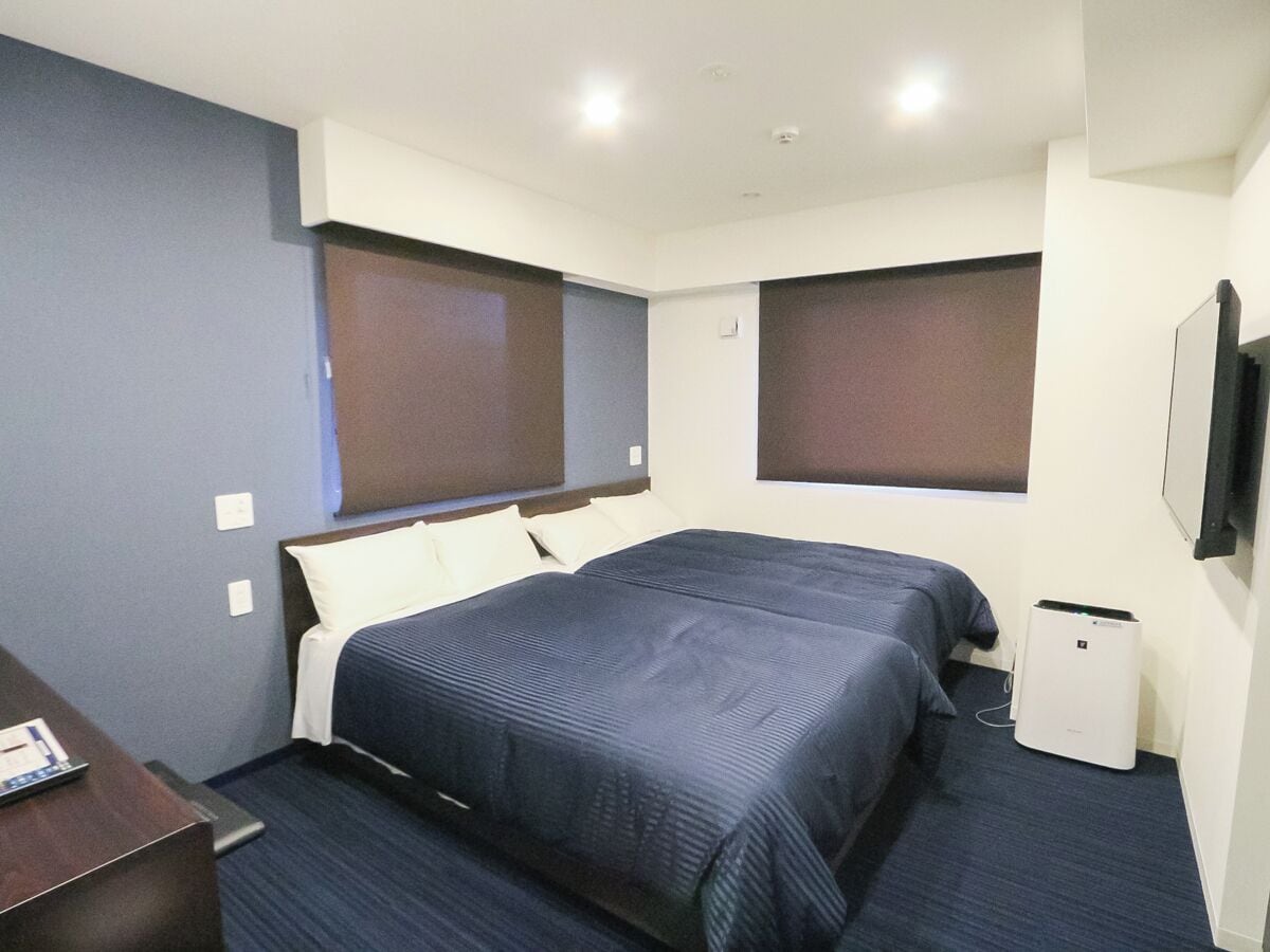 A hotel room with a bed, bedside table, and a TV mounted on the wall.