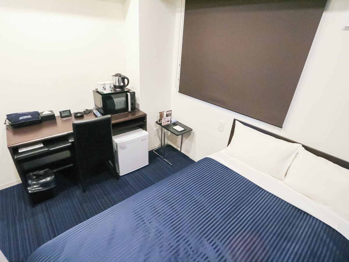 A hotel room with a bed, desk, microwave, refrigerator, and a small table with a phone and a cup.