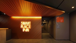 Un área de recepción con un cartel que dice 'SMART PLACE IN', techo de listones de madera y un pasillo que lleva a las habitaciones.