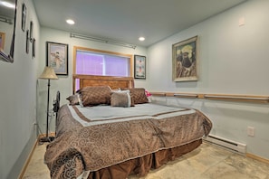 A bedroom with a bed, a window with blinds, a standing lamp, and wall-mounted artwork. - Quaint Juneau Apt w/ Scenic Mountain Surroundings! (Juneau)