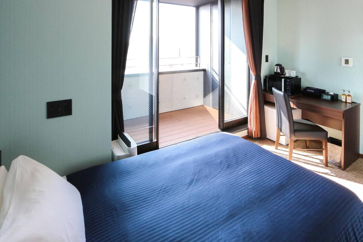 A hotel room with a bed, a desk, and a view of the balcony.