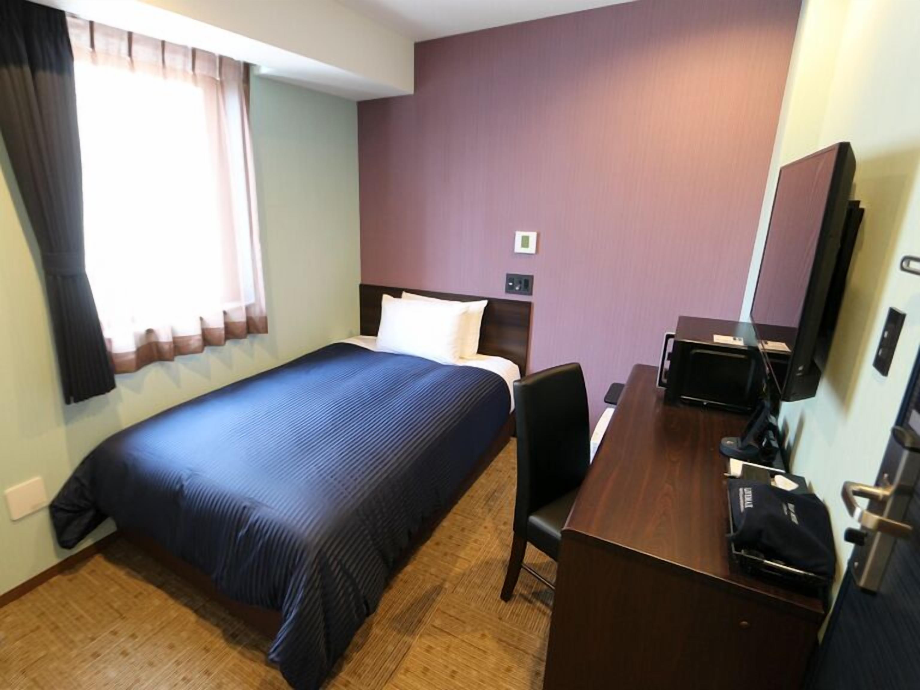 A hotel room with a bed, a desk, a chair, a television, and a window with curtains.
