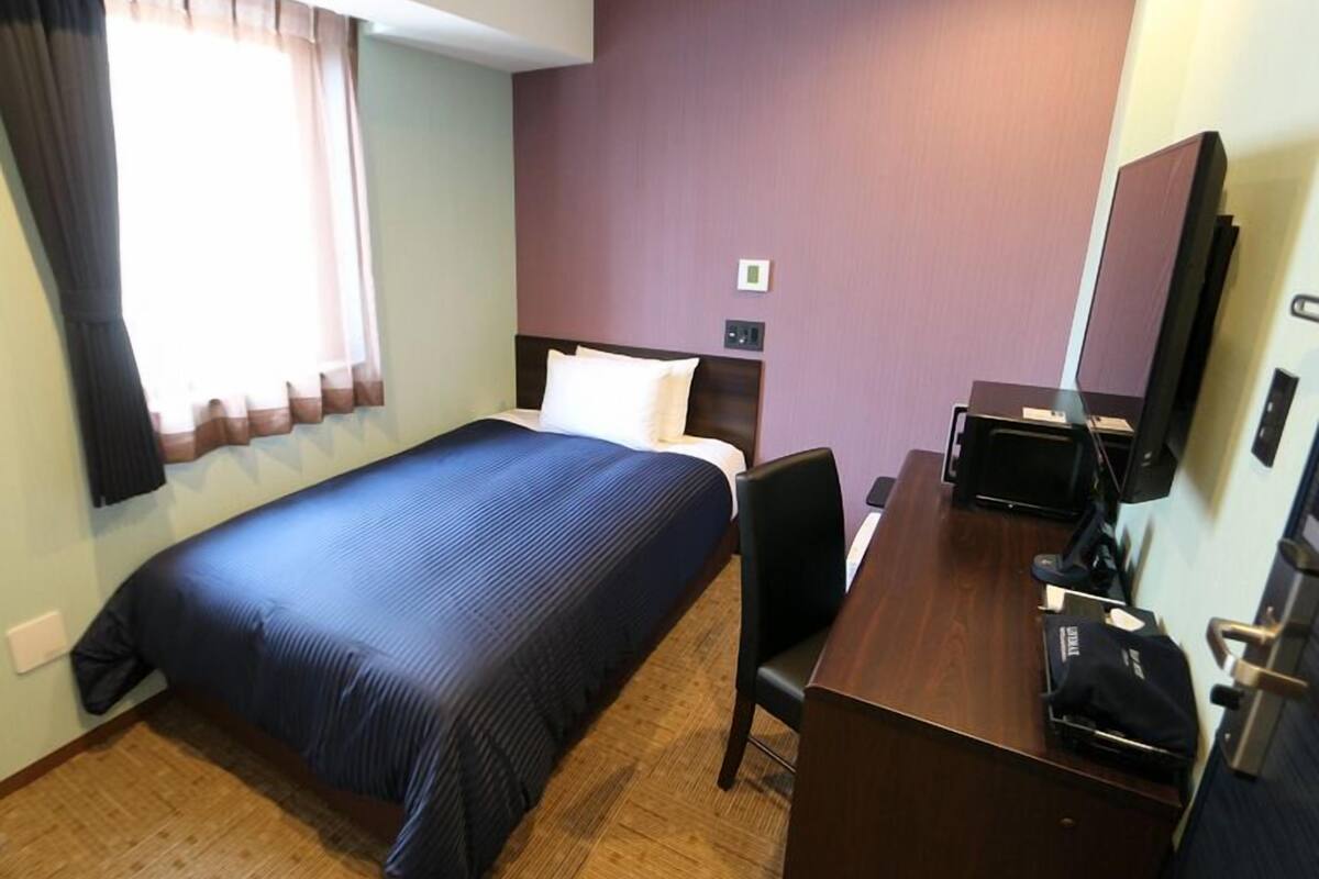 A hotel room with a bed, a desk, a chair, a television, and a window with curtains.