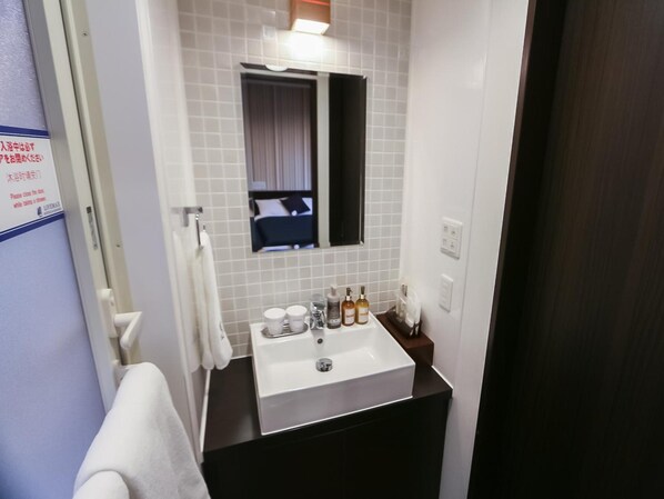 Une salle de bain avec un lavabo blanc, deux flacons de savon pour les mains, un miroir et un porte-serviettes.