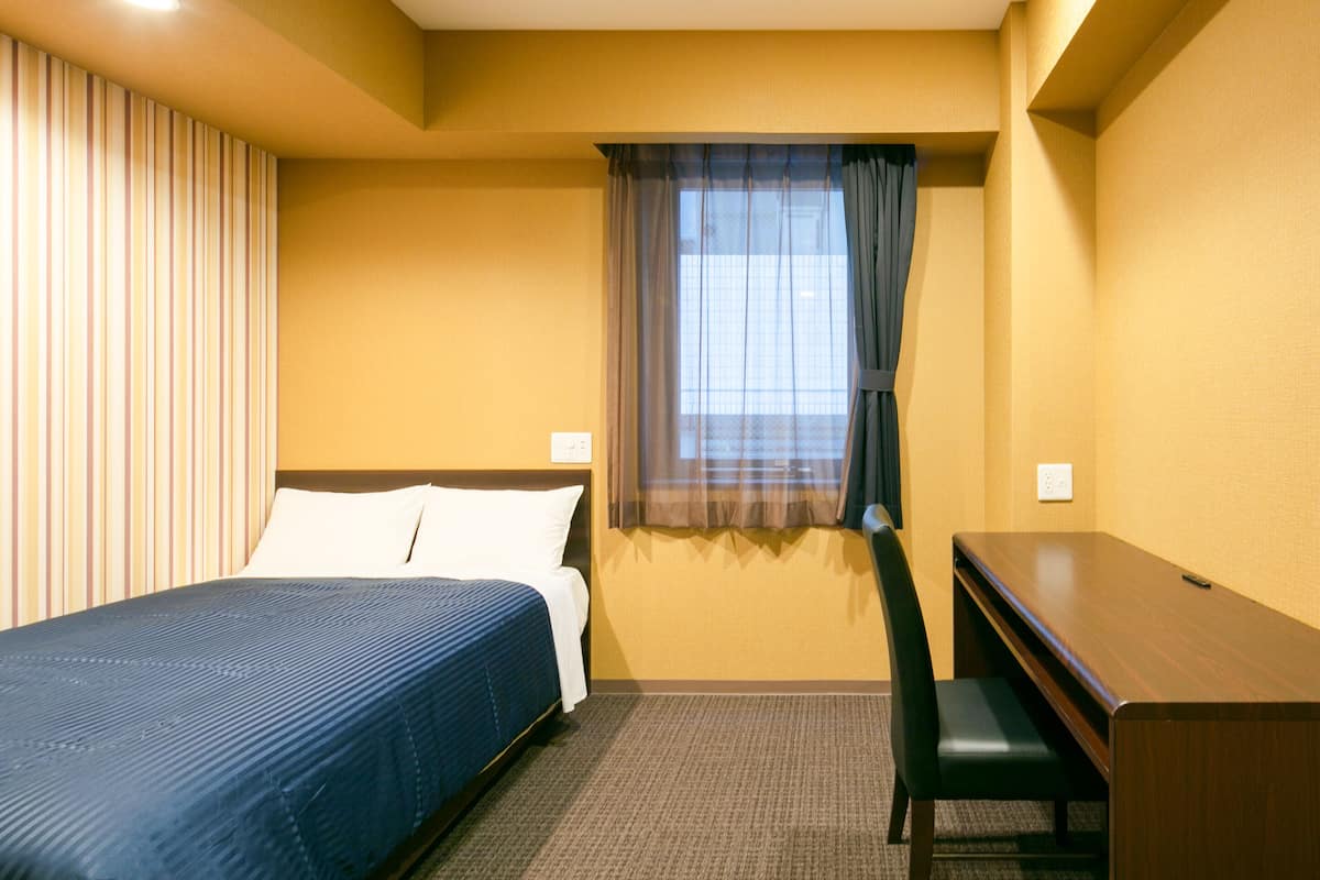 A hotel room with a bed, a desk, and a window with curtains.