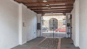 A covered hallway with a metal gate, a brick pathway, and a red car visible through the gate.