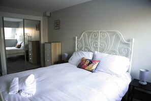 Un lit bien fait, avec des draps blancs, un coussin coloré et une paire de serviettes.