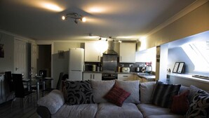 A living room with a sofa, a dining table with chairs, and a kitchen area with cabinets and appliances.