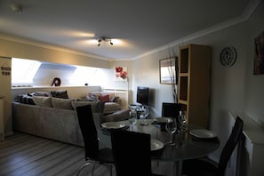 A compact living space with a dining area, a sofa, a TV, and a clock on the wall. - The Stables: Fabulous stylish flat in Merchant City & Parking (Glasgow)