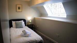 A bedroom with a bed, a nightstand, a lamp, a framed picture, and a skylight.