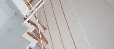 A modern staircase with wooden steps and white railings, leading to a higher floor.