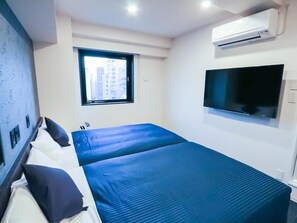 A hotel room with a bed, a TV mounted on the wall, and an air conditioning unit.