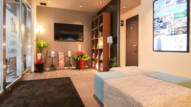 A modern hotel room with a flat-screen TV mounted on the wall, a bookshelf, a small table with a potted plant, and a large window. - Hotel Livemax Tokyoshintomicho (Tokyo)