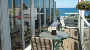 Un espace extérieur abrité, doté d’une table et de chaises, de grandes fenêtres et offrant une vue sur l’océan.