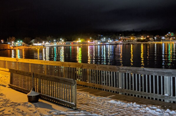 A nighttime view of a waterfront area with a wooden walkway and snow on the ground.