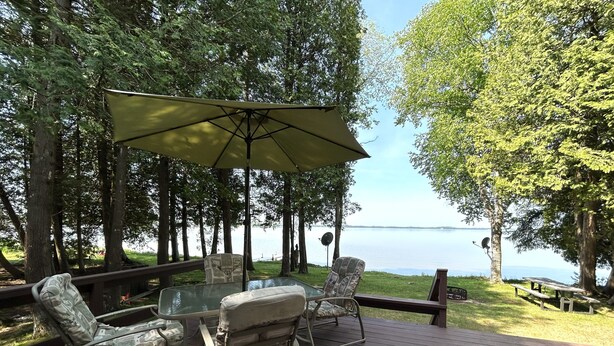 A deck with outdoor furniture, including chairs and a table, overlooking a body of water. - The House that Jack Built (Moran)