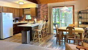A kitchen with wooden cabinets, a refrigerator, a sink, and a dining area with a table and chairs. - The House that Jack Built (Moran)