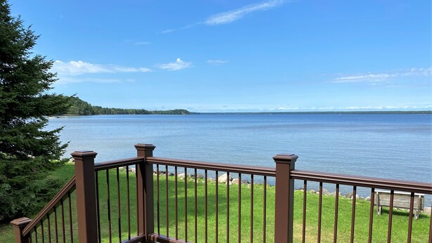 A wooden deck with a brown railing overlooking a calm lake with a distant shoreline.