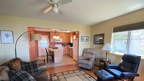 A living room with a sofa, a chair, a rug, and a view of the kitchen and dining area.