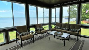 A sunroom with large windows overlooking a body of water, furnished with a sofa and chairs, and a small table.