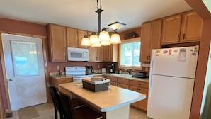 A kitchen with wooden cabinets, a white refrigerator, a microwave, a stove, and a dining area with two chairs.
