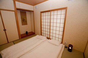 A traditional Japanese-style room with tatami flooring, a low bed with a wooden headboard, and sliding doors. - Koueki (Kyoto)