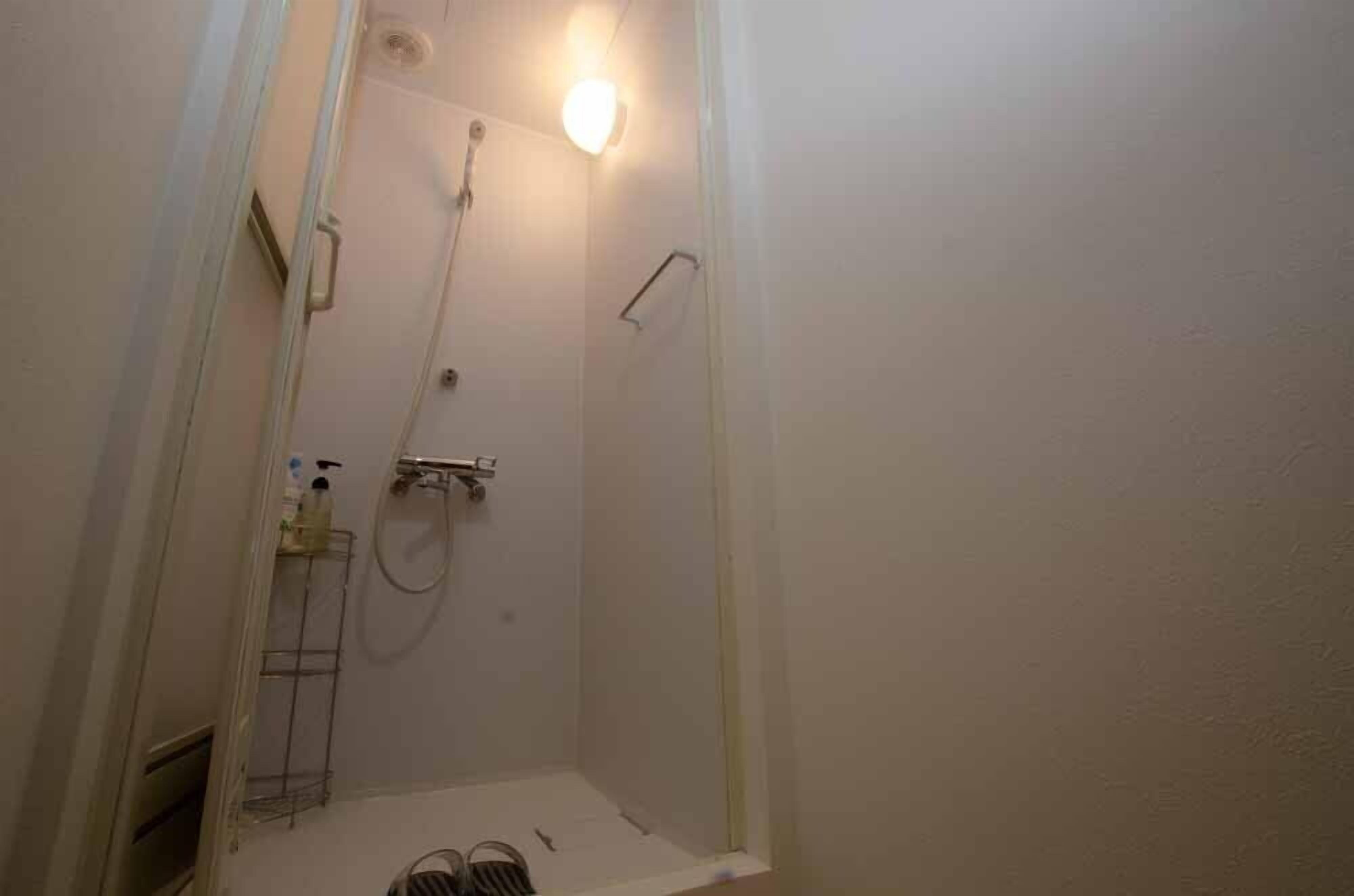 Een kleine, afgesloten douchecabine met een handdouche, een handdoekhouder en een plank met toiletartikelen.