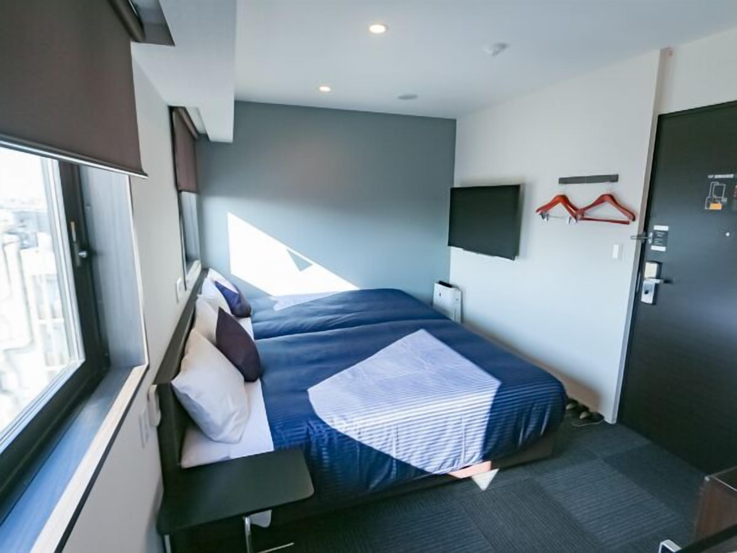 A bedroom with a bed, a desk, a TV, and a door.