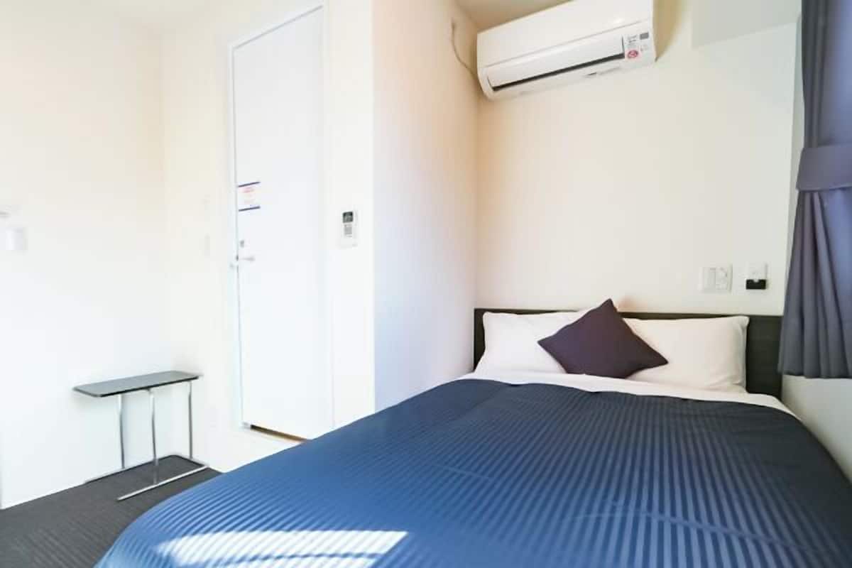 Ein Hotelzimmer mit Bett, kleinem Tisch, Klimaanlage und einer Tür.