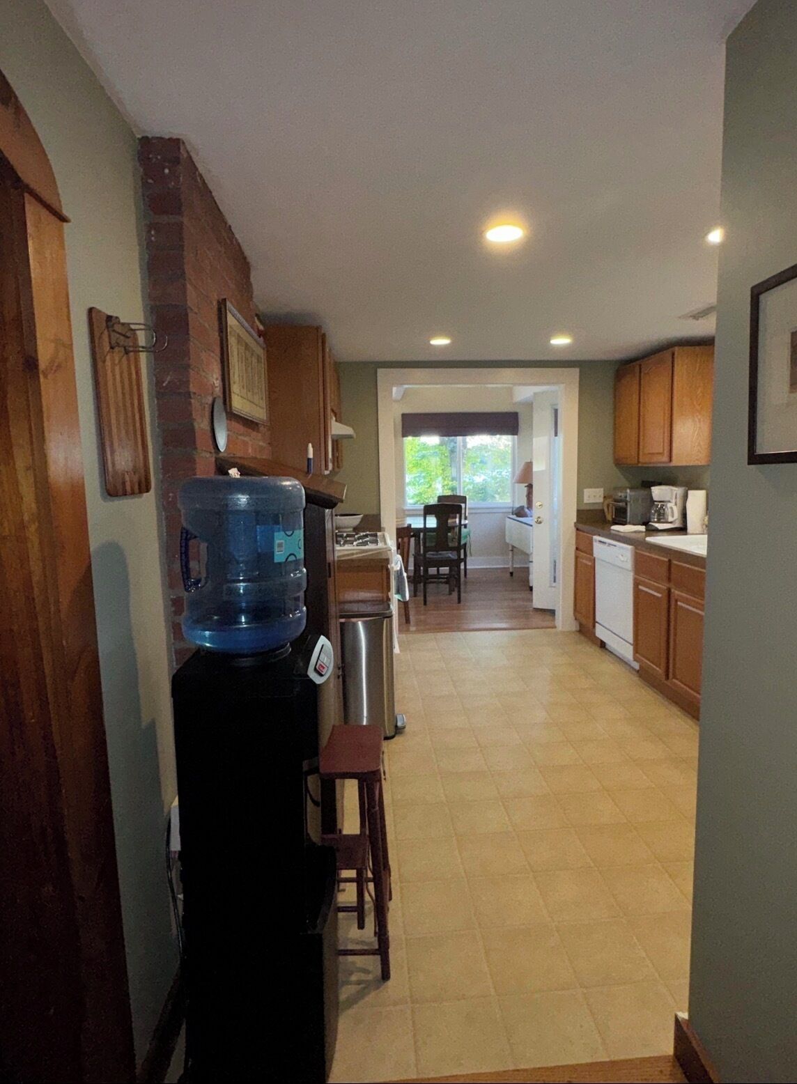 A kitchen with a water dispenser, cabinets, and a dining area with chairs.