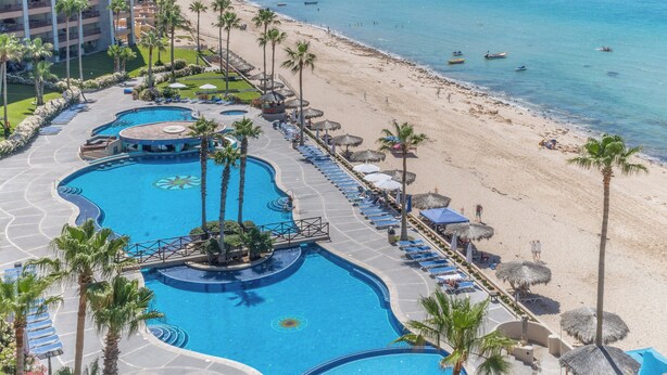 Ein Resort mit großem Schwimmbad, Strand und Palmen.
