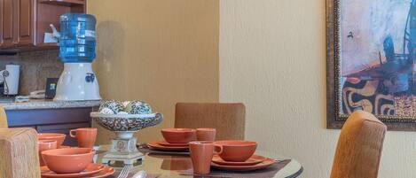 Un coin repas avec une table en verre, de la vaisselle orange et un bol décoratif.