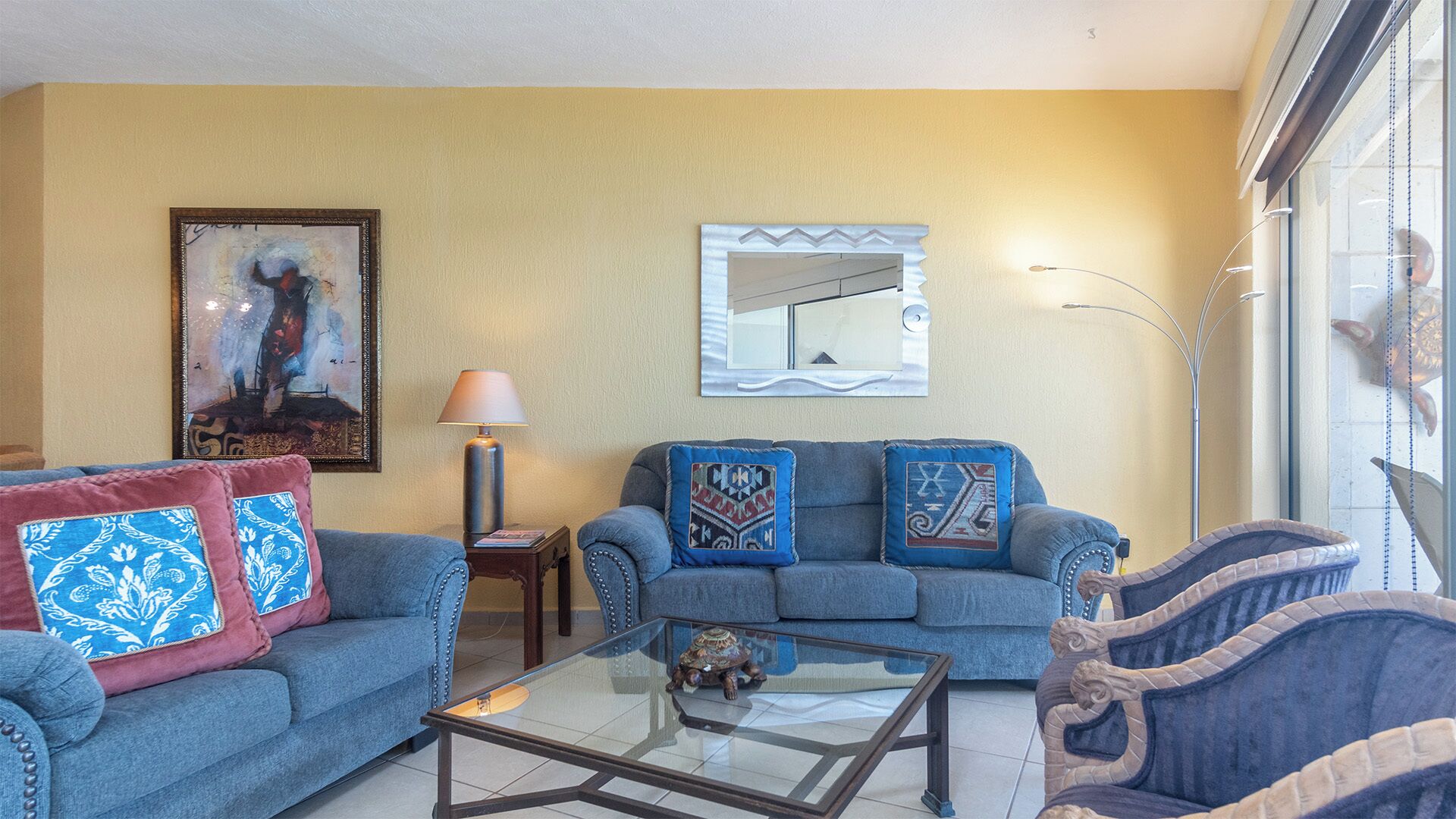 Un salon comprenant un canapé, un fauteuil et une table basse, agrémenté de coussins à motifs et d’une œuvre d’art encadrée accrochée au mur.