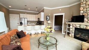 A living room with a glass coffee table, orange sofa, and a fireplace with a stone mantle.