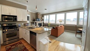 A modern kitchen with stainless steel appliances, a stone fireplace, and a large window overlooking a residential area.