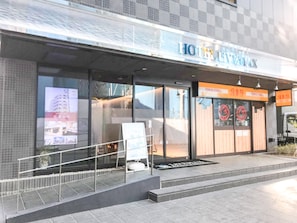 A hotel entrance with a glass facade, a visible signboard, and a staircase leading up to the entrance. - Hotel Livemax Chiba Station (Chiba)