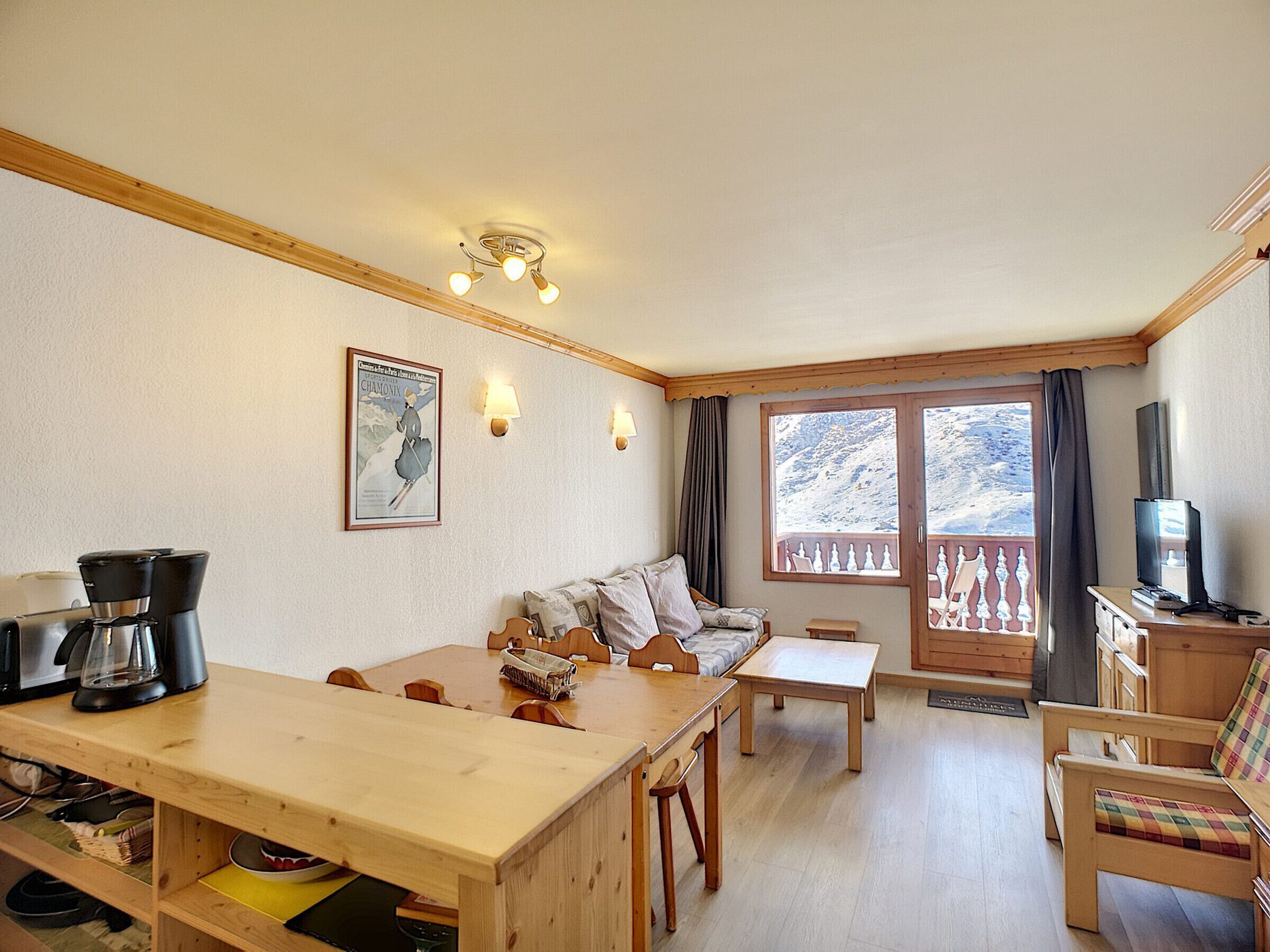 A cozy room with a wooden dining table, sofa, and a TV on a wooden cabinet.