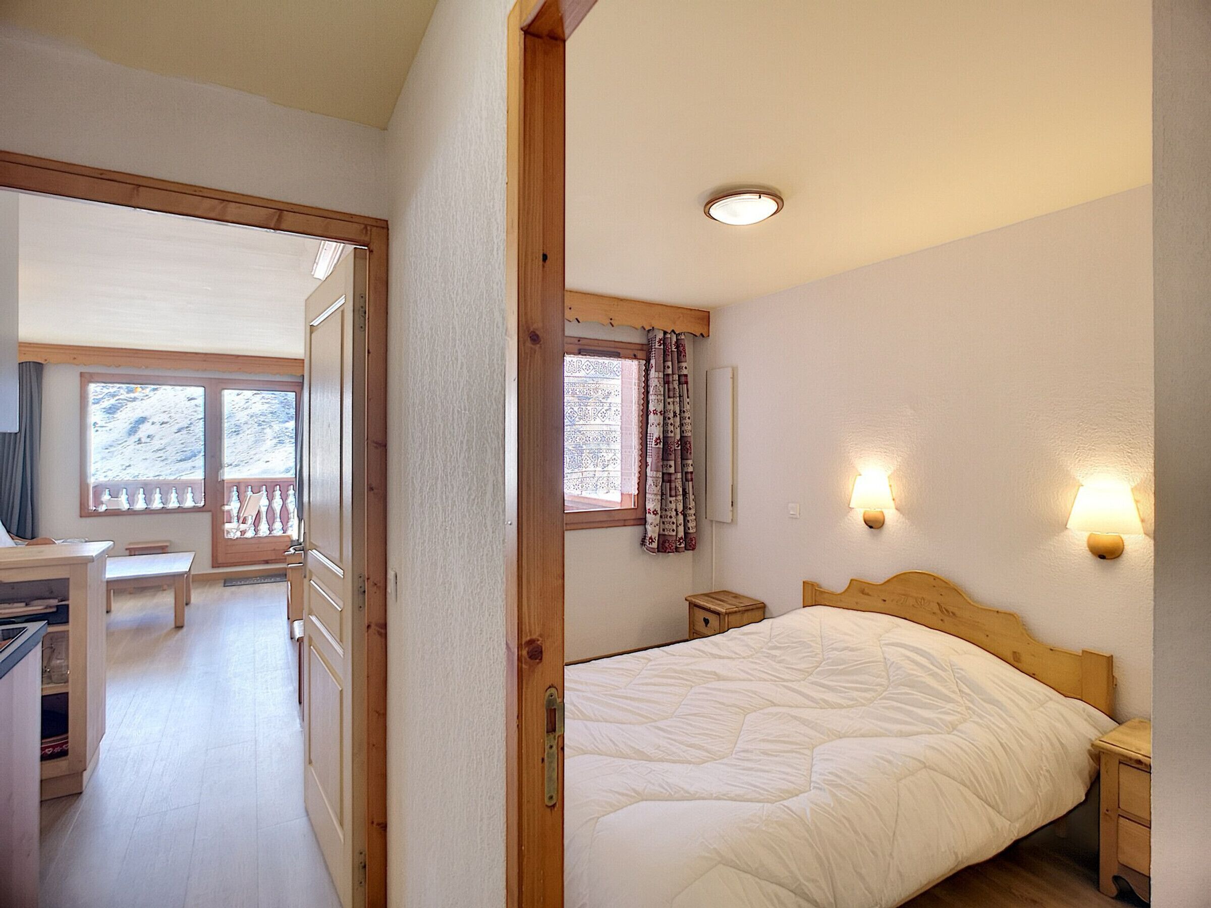 A bedroom with a bed, bedside tables, a desk, and a chair. There is a window with curtains and a view of the outside.
