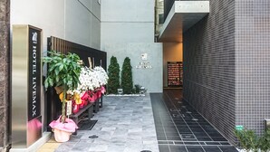 A hotel entrance with a modern design, featuring a metal gate, a bench with potted plants, and a sign for the hotel. - HOTEL LiVEMAX Tokyo-Otsuka Ekimae (Tokyo)