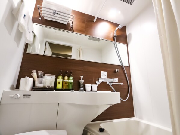 Une salle de bain avec un lavabo blanc, un miroir, une douche et des articles de toilette posés sur le comptoir.