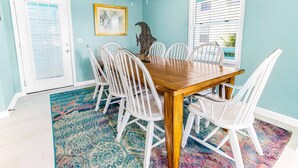 A dining room with a wooden table and white chairs, a colorful rug, and a ceiling fan. - Coastal Tybee House & Bungalow : Steps from Beach (Tybee Island)
