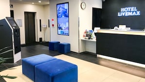 Ein Hotel-Empfangsbereich mit einem schwarzen Empfangsschalter, einem digitalen Bildschirm, der Hotelinformationen anzeigt, einer Uhr und blauem Sitzmöbel.