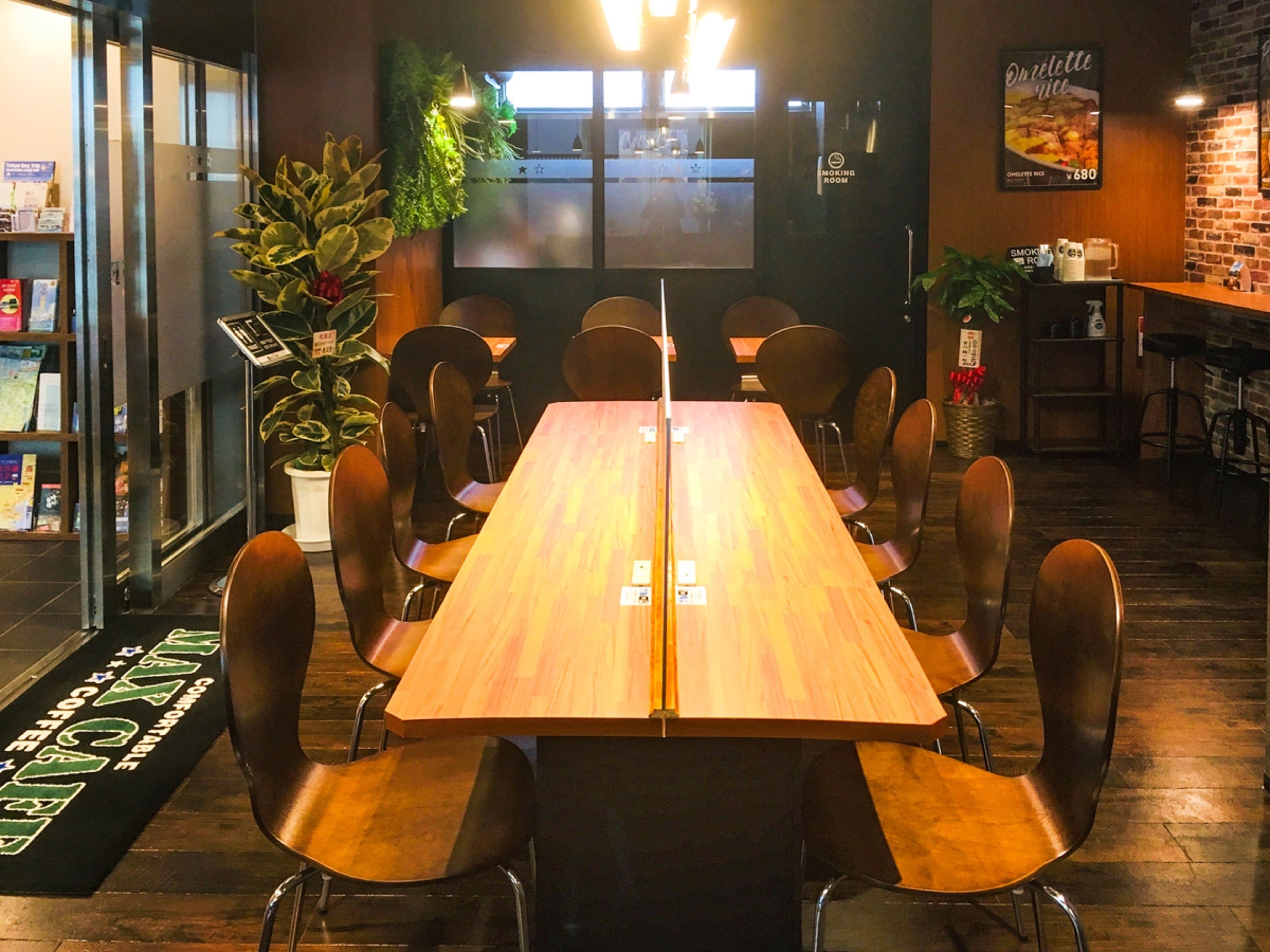 A restaurant with a long wooden table and multiple chairs. There is a bar area with stools and a menu board on the wall.