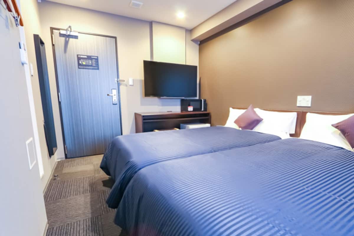 Habitación de hotel con dos camas, un televisor en la pared y una puerta con un cartel.