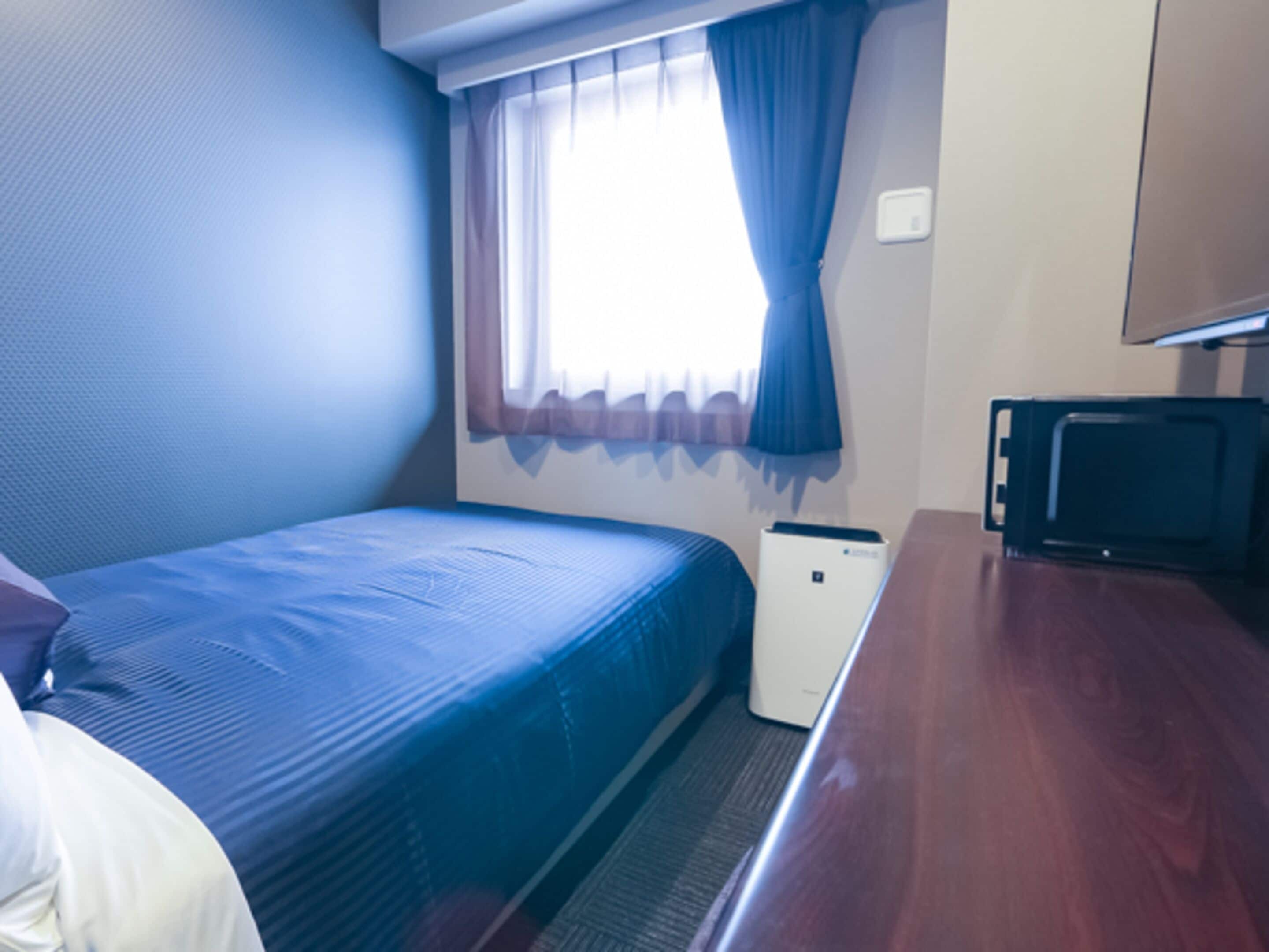 A compact hotel room with a single bed, a small desk, a television, and a window with curtains.