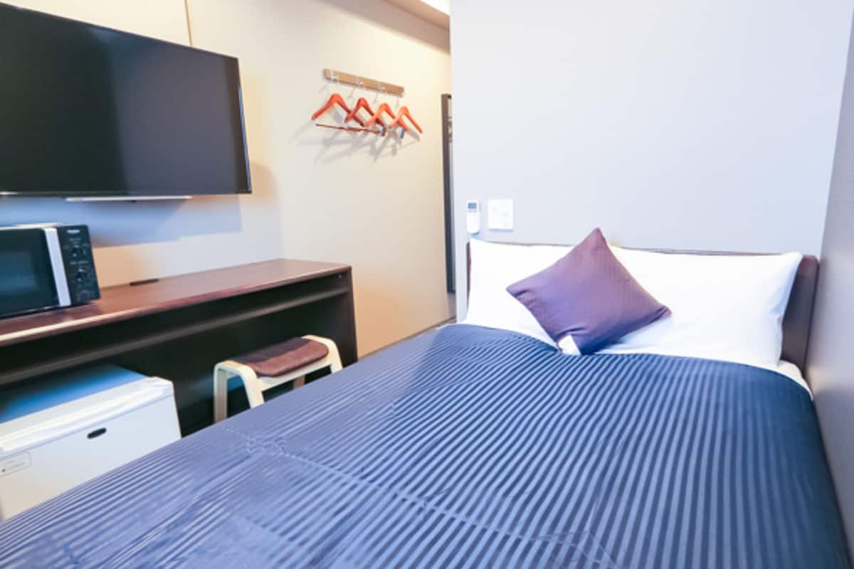 Una habitación de hotel con una cama, televisor, microondas y un escritorio pequeño.