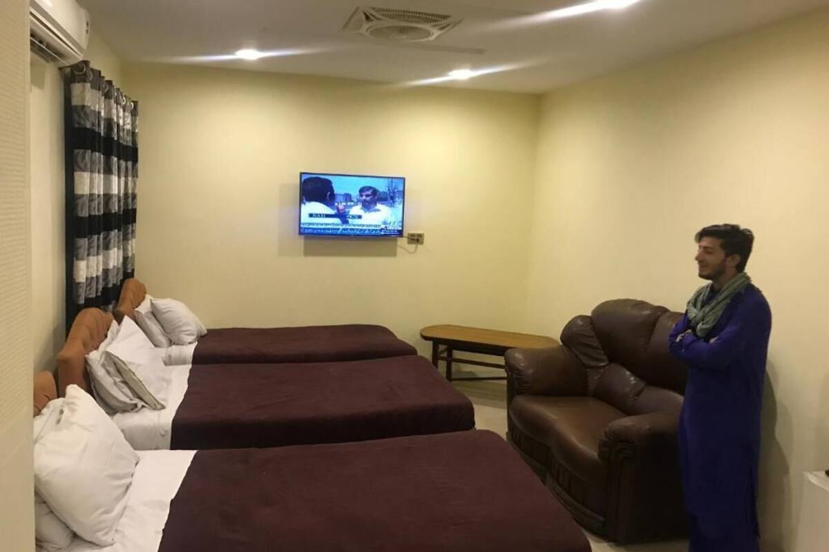 Une chambre d’hôtel avec deux lits, une télévision, un canapé en cuir et une petite table.