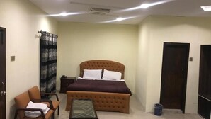 A bedroom with a bed, a chair, a table, and a door. - National City Hotel (Rawalpindi)